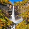 Kegon Falls dropping between steep cliffs surrounded by red, orange and yellow autumn foliage.