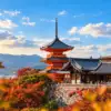 A red pagoda and temple buildings at Kiyomizu-dera surrounded by colourful autumn trees in Kyoto.