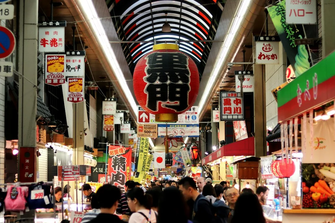 A busy covered shopping arcade beneath a large Kuromon lantern at Kuromon Ichiba Market in Osaka.