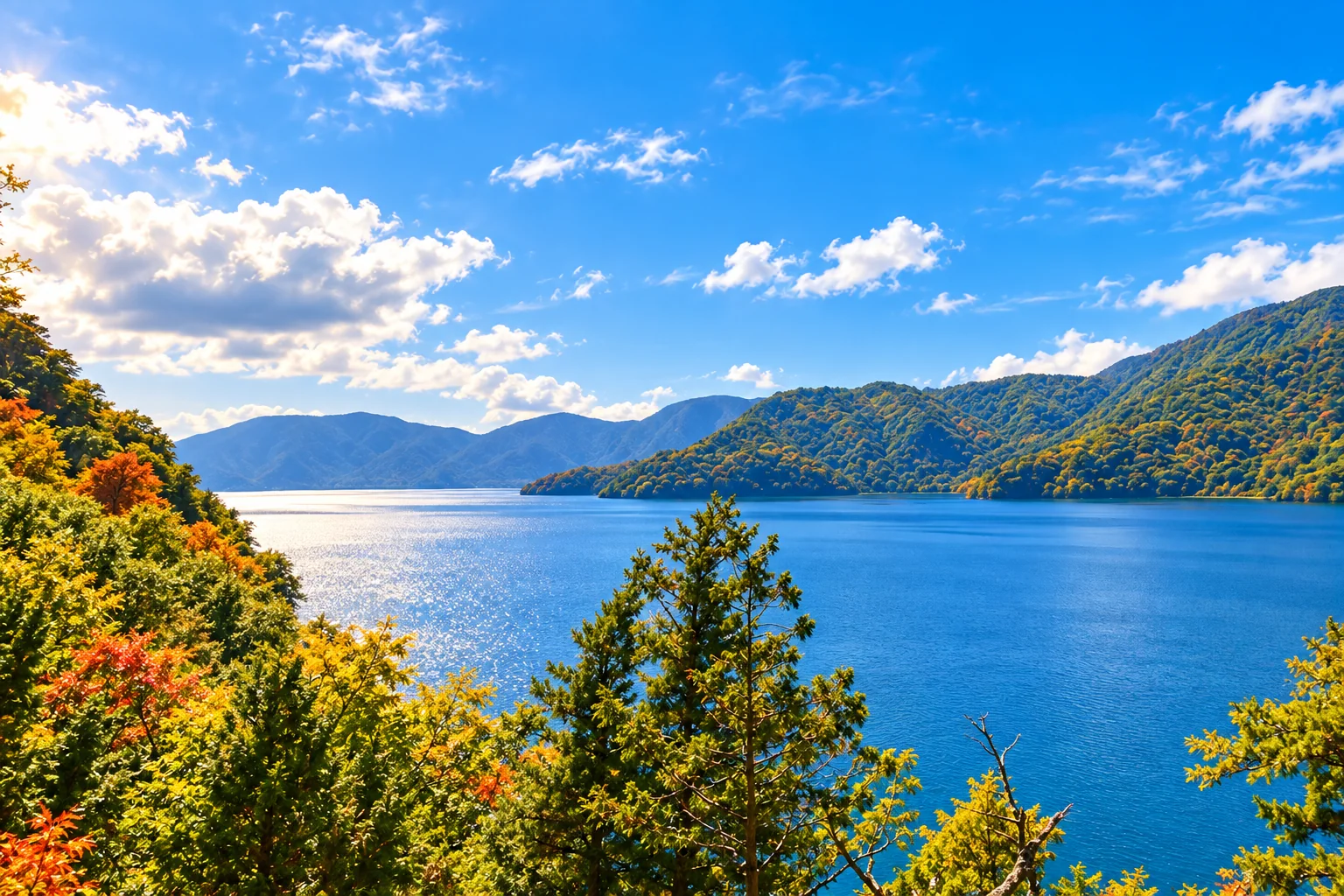 Blue water at Lake Chuzenji bordered by forested mountains and autumn-coloured trees.
