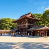 Visitors in a sunlit courtyard beside traditional shrine buildings at Meiji Shrine in Tokyo.