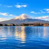Snow-capped Mount Fuji beyond the blue water and shoreline of Lake Kawaguchi.