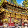 An ornate red and gold temple gate with decorative carvings and stone lanterns in Nikko.