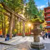 A five-storey red pagoda, stone torii gate and lantern among tall trees at Toshogu Shrine in Nikko.